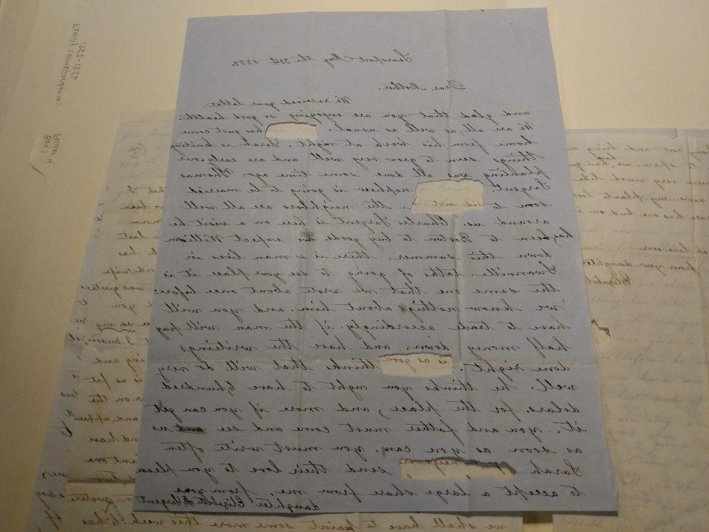 Color photograph of several black ink handwritten letters piled on top of each other. They have oval or rectangular ripped out sections, about the size of one word. 